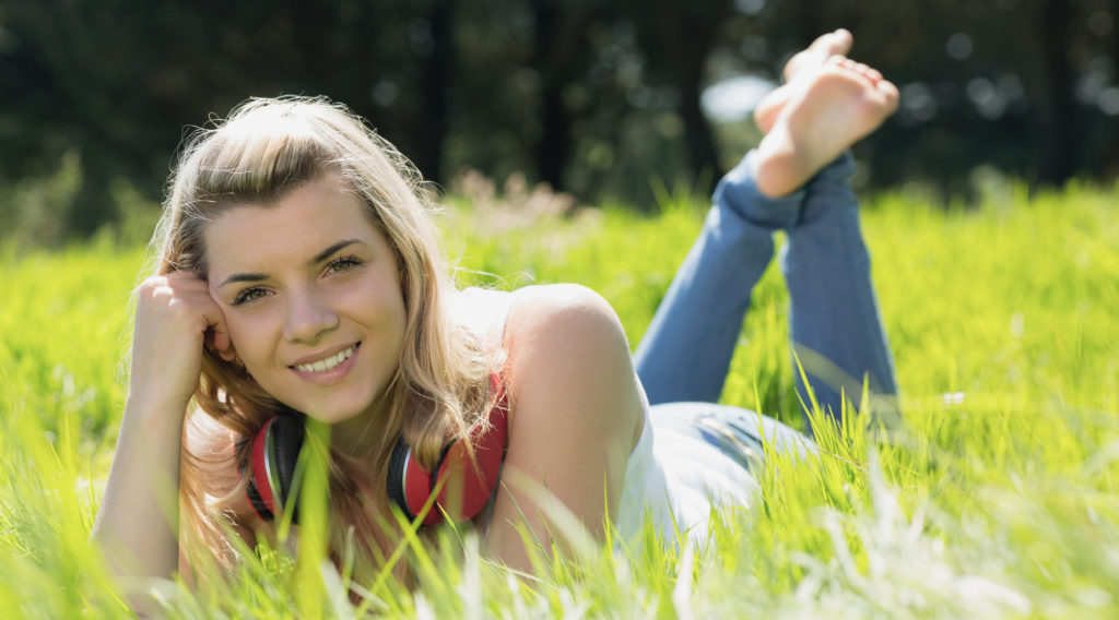 Pretty blonde lying on grass with headphones around neck on a sunny day in the countryside