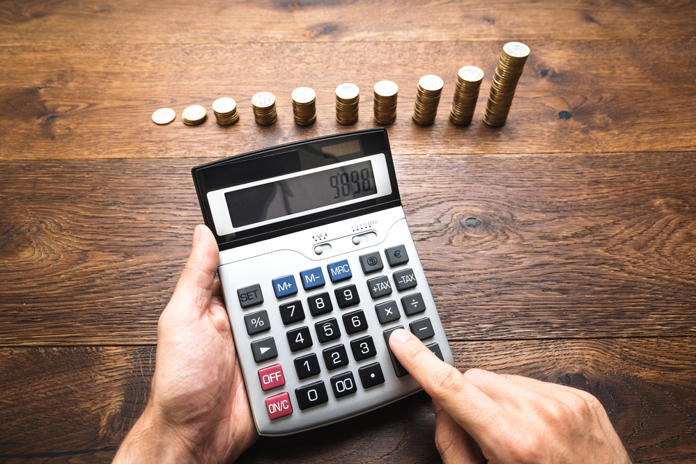 Businessman Doing Calculations In Front Of Stacked Coins