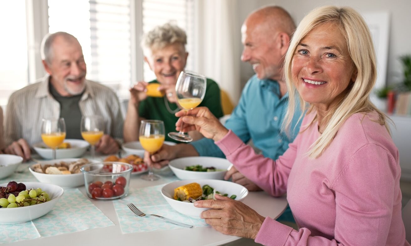 Group of senior friends having party indoors, talking when eating at the table.