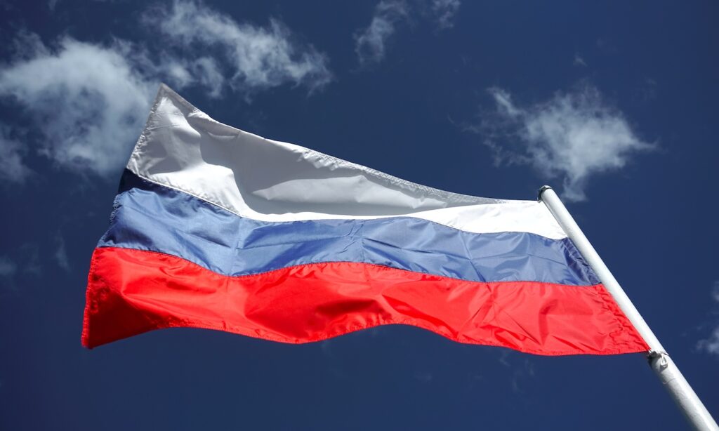Russian tricolor flag waving in the wind against a blue sky. Russian flag on blue cloudy sky background