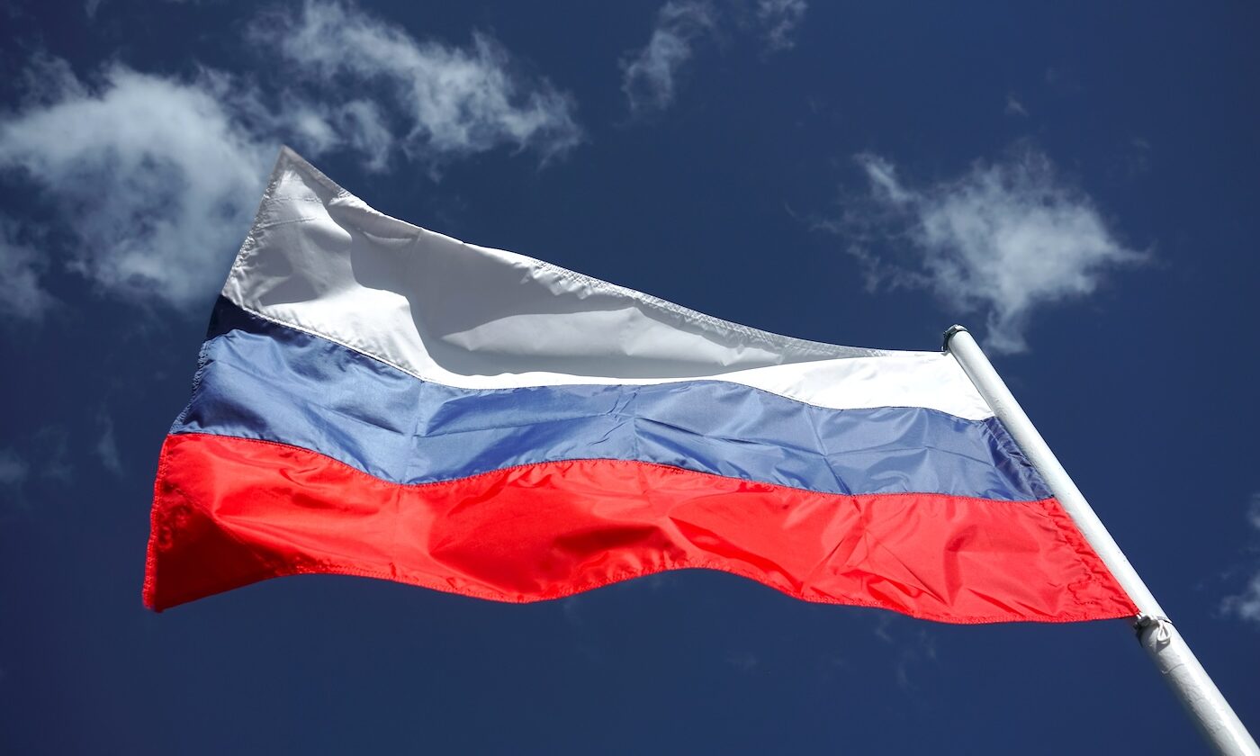 Russian tricolor flag waving in the wind against a blue sky. Russian flag on blue cloudy sky background