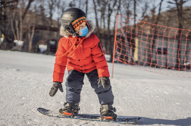 Kind mit Maske auf Snowboard
