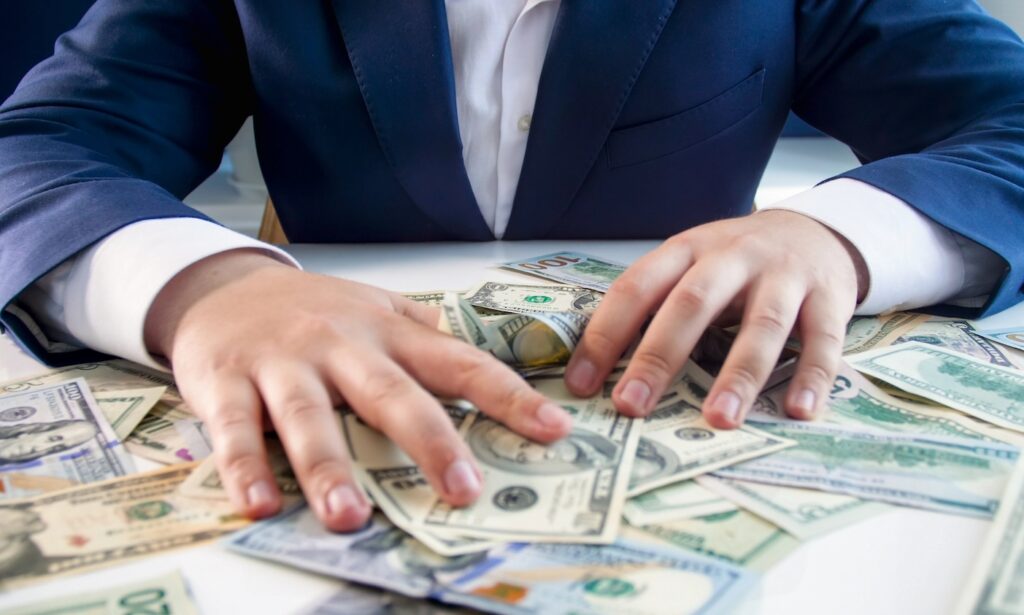 Conceptual photo of greed and avarice. Businessman grabbing money lying on office desk