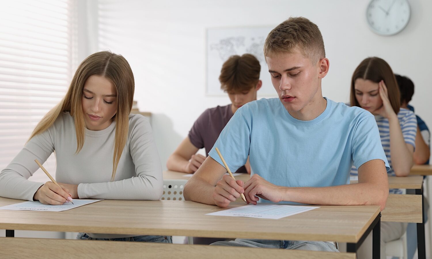 Students taking exam at wooden table indoors